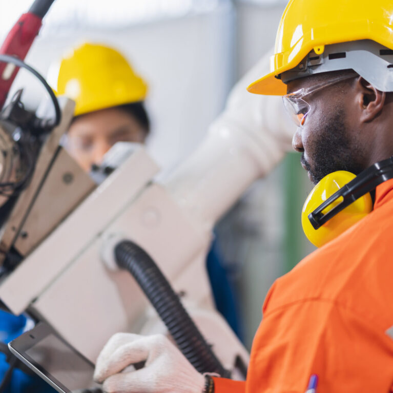 engineer cooperation male and female technician maintenance control relay robot arm system welding with tablet laptop to control quality operate process work heavy industry 4.0 manufacturing factory